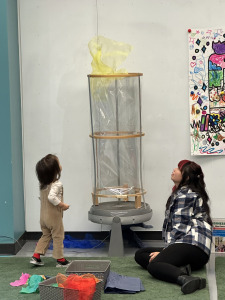 Adult and child playing with scarves in a wind tunnel. 