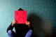 Adult holding a piece of red paper in front of their face with a frown drawn upon it.