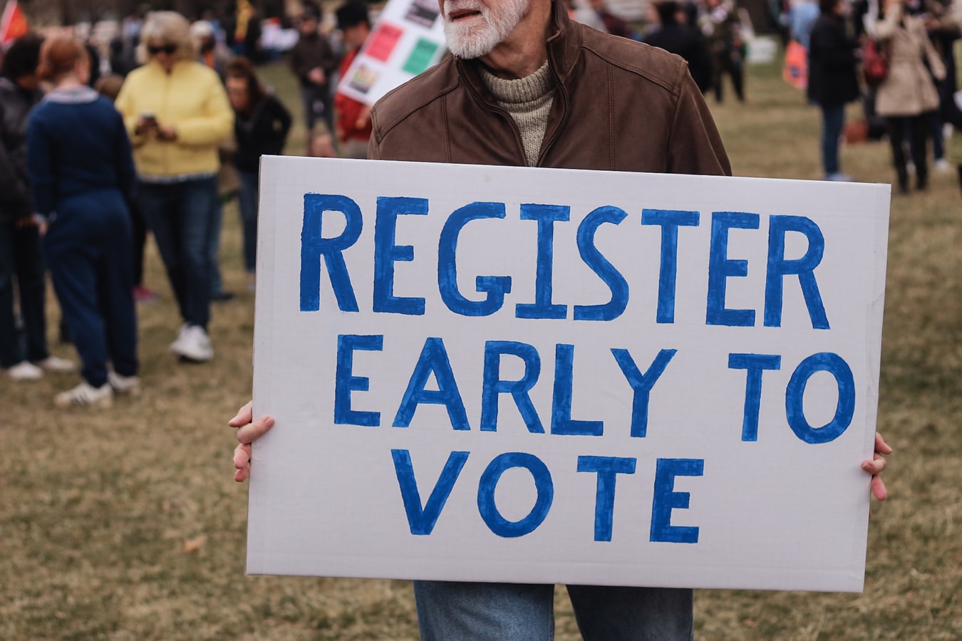 Man holding a sign that reads register early to vote.