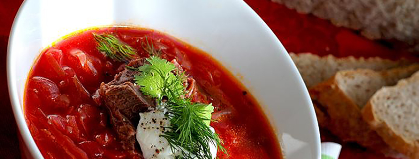 A white bowl is depicted containing borsch, a beet based soup that is reddish in color.