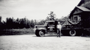 Black and white picture of a man standing by an old truck